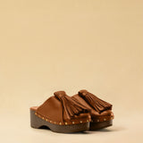 Clogs CHOUCHA in Cognac by LABEL17, crafted from supple, vegetable-tanned lamb nappa leather. A large, soft pompom on top swings elegantly from left to right with each step, adding a playful yet refined touch. The shoe features a durable sole for comfort and stability. The artisanal craftsmanship enhances the overall aesthetic, making these clogs a true statement piece. Quiet luxury at its best. Handmade in Greece.