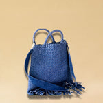 Die Crossbody Bag Tresse Fringes Denim von LABEL17 mit geflochtenen Henkeln und langem abnehmbarem Schulterriemen, ist aus gewaschenem Denim gefertigt und von Hand geflochten.