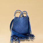 Die Crossbody Bag Tresse Fringes Denim von LABEL17 mit geflochtenen Henkeln und langem abnehmbarem Schulterriemen, ist aus gewaschenem Denim gefertigt und von Hand geflochten.