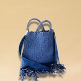 Die Crossbody Bag Tresse Fringes Denim von LABEL17 mit geflochtenen Henkeln und langem abnehmbarem Schulterriemen, ist aus gewaschenem Denim gefertigt und von Hand geflochten.