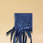 Die Crossbody Bag Tresse Fringes Denim von LABEL17 mit geflochtenen Henkeln und langem abnehmbarem Schulterriemen, ist aus gewaschenem Denim gefertigt und von Hand geflochten.