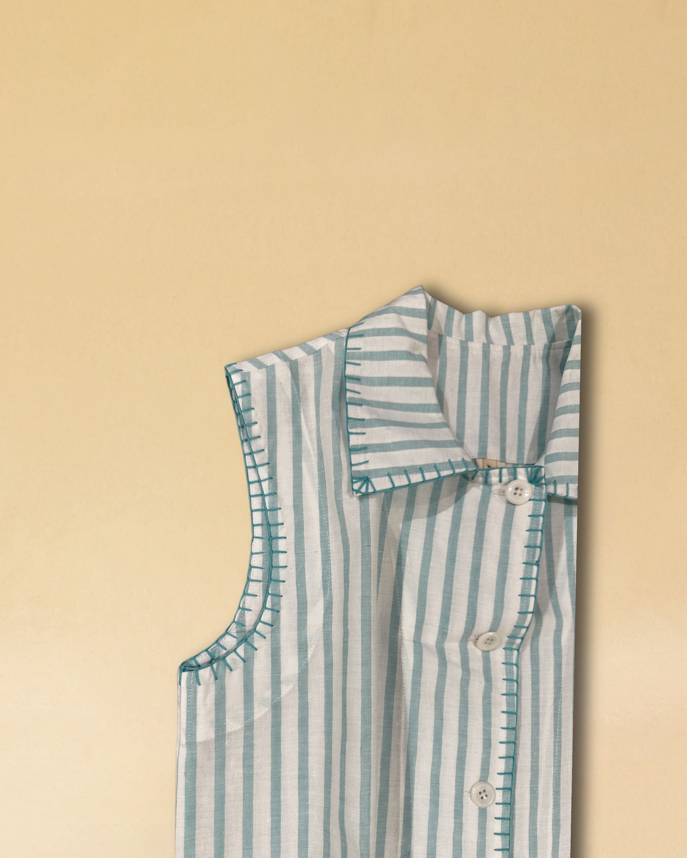 Unsere Vest LINDA aus hochwertiger Baumwolle ist eine ärmellose Veste, veredelt mit einem handgenähten Zierstich (Hbik-Stitch) in Türkis entlang der Knopfleiste, dem Kragen und dem Armloch.