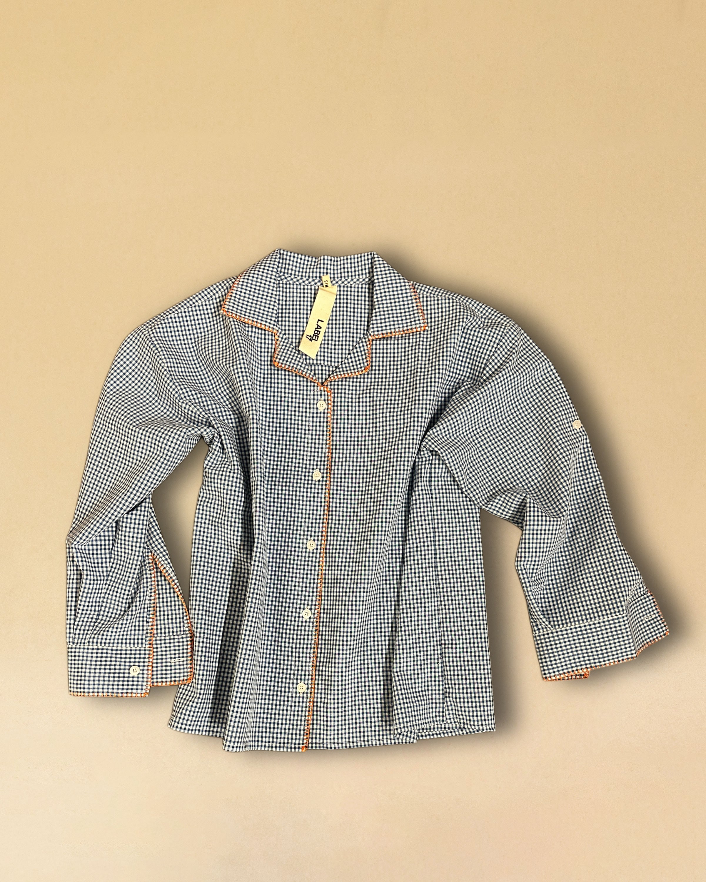 Die Blouse LARA von LABEL17 aus hochwertiger Baumwolle im klassischen Blau-Weiss Vichy-Karo-Muster hat einen Reverskragen , veredelt mit einem handgenähten Zierstich (Hbik-Stitch) in Orange entlang dem Reverskragen, der Knopfleiste und der Manschette.