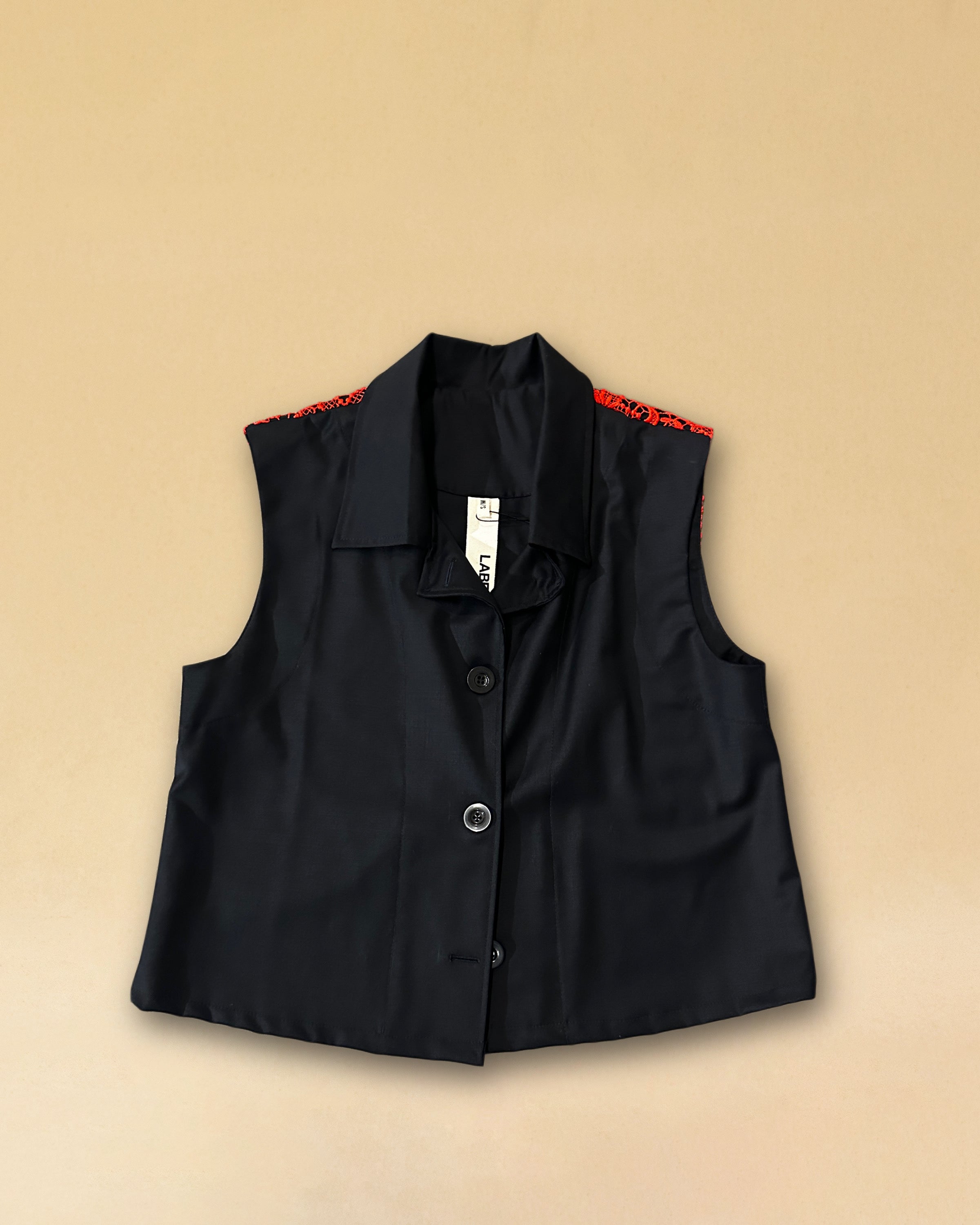 Die Vest LACE in Night Blue aus hochwertigem Baumwollmischgewebe besticht durch ihre elegante Spitzenapplikation in Rot auf dem Rücken – ein kühnes Detail, das dem schlichten Gilet eine dramatische Note verleiht. Knopfverschluss und ärmelloser Schnitt machen sie zum vielseitigen Stück für besondere Anlässe.