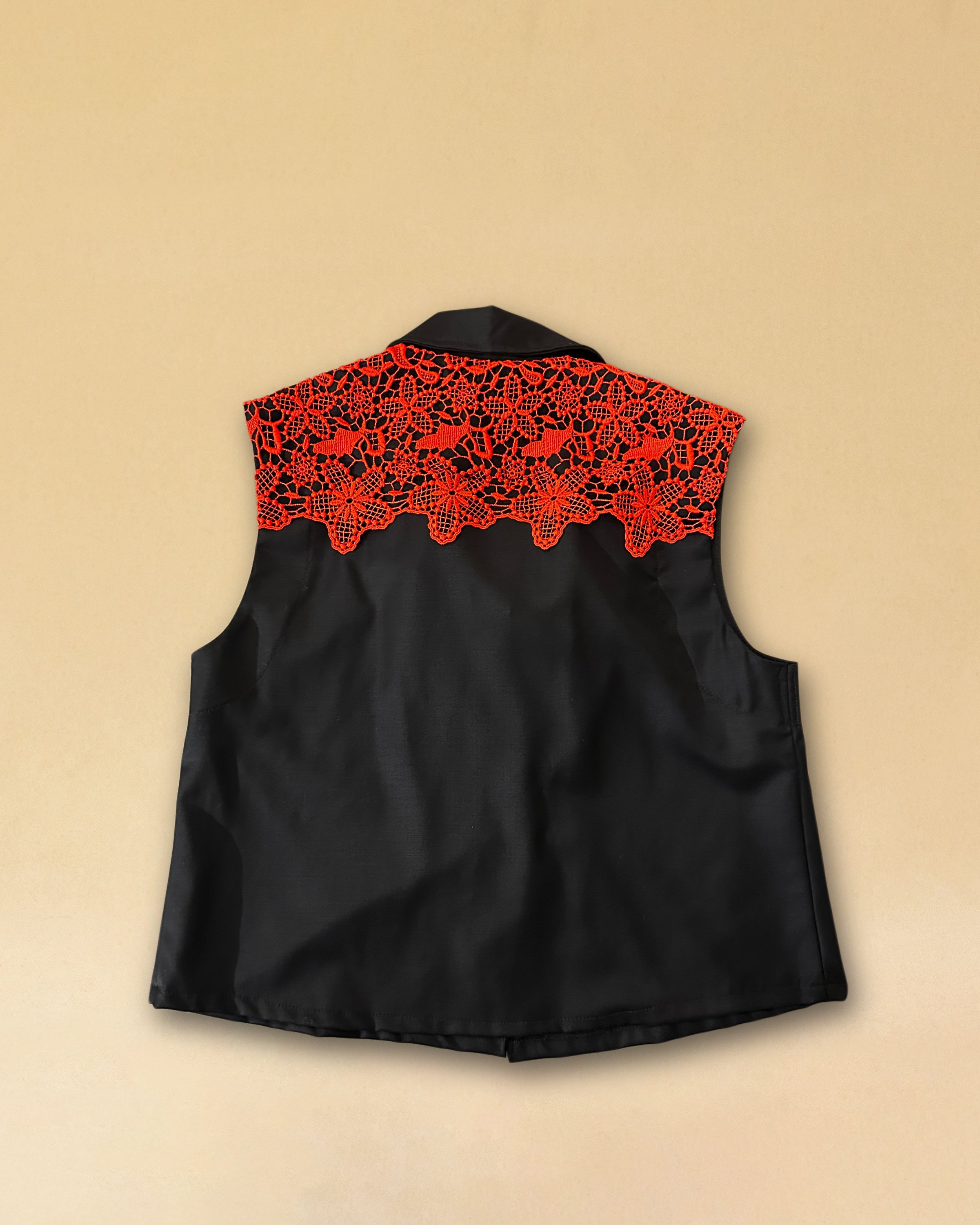 Die Vest LACE in Night Blue aus hochwertigem Baumwollmischgewebe besticht durch ihre elegante Spitzenapplikation in Rot auf dem Rücken – ein kühnes Detail, das dem schlichten Gilet eine dramatische Note verleiht. Knopfverschluss und ärmelloser Schnitt machen sie zum vielseitigen Stück für besondere Anlässe.