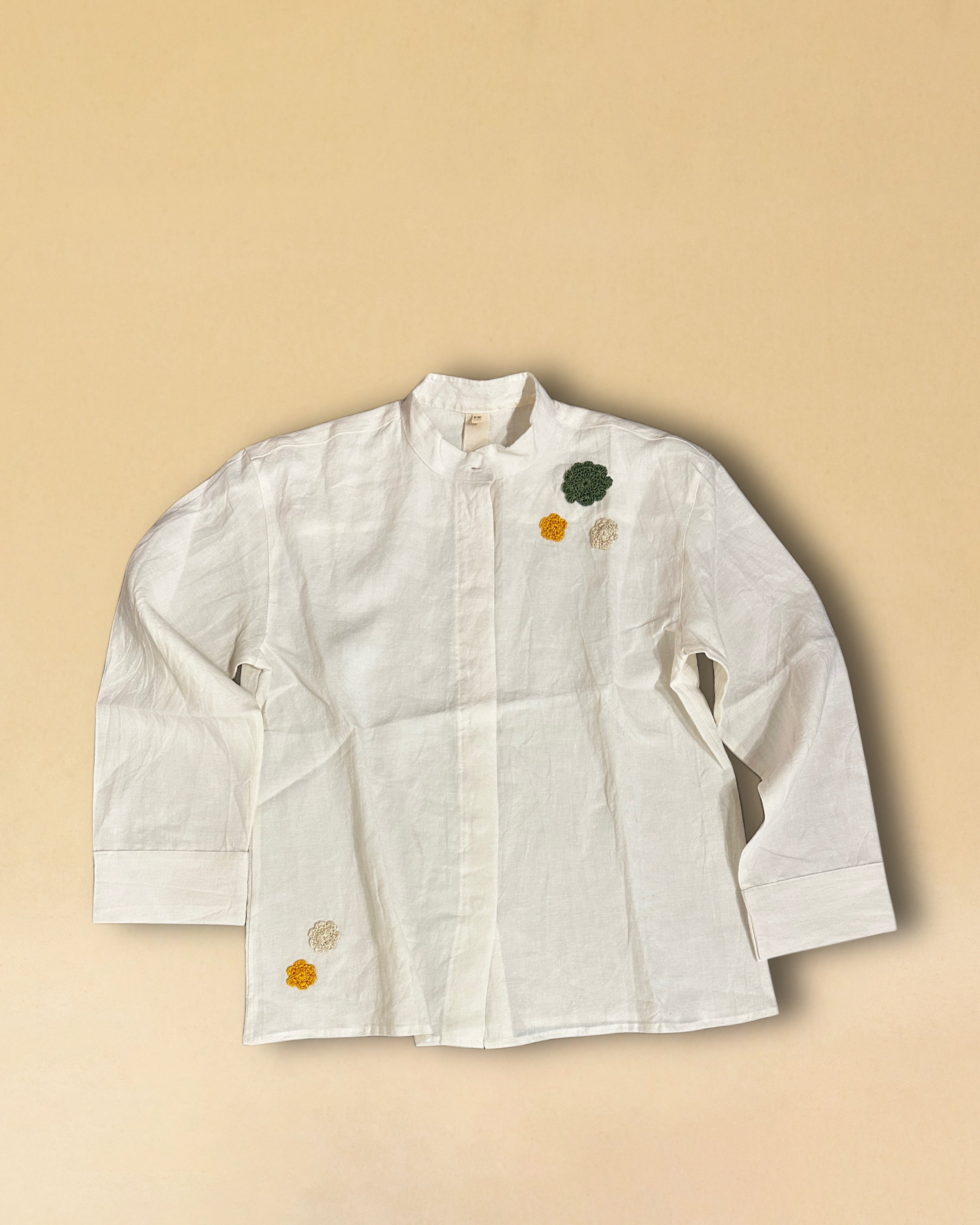 LABEL17's Blouse MANDY hat einen Stehkragen und eine gedeckte Knopfleiste aus einem leichten Baumwoll-Leinen-Mischgewebe – angenehm auf der Haut und ideal für warme Tage. Veredelt mit fünf handgehäkelten Blumen in verschiedenen Grössen und Farben – drei im Brustbereich und zwei unten rechts.