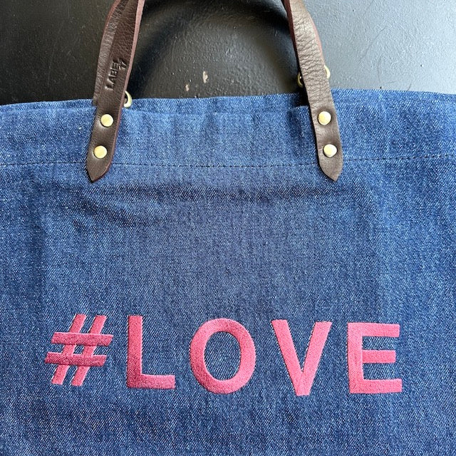 Bestickte Stofftasche von LABEL17 mit braunen Lederhenkeln und #LOVE Botschaft auf der Vorderseite. Hergestellt in Marokko