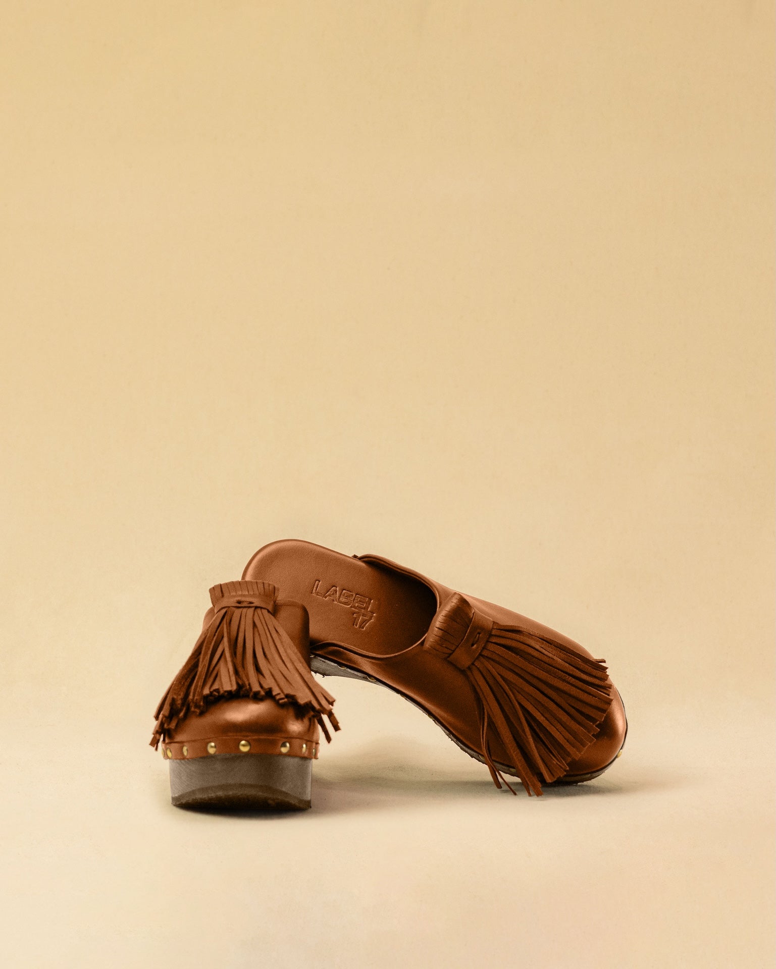 Clogs CHOUCHA in Cognac by LABEL17, crafted from supple, vegetable-tanned lamb nappa leather. A large, soft pompom on top swings elegantly from left to right with each step, adding a playful yet refined touch. The shoe features a durable sole for comfort and stability. The artisanal craftsmanship enhances the overall aesthetic, making these clogs a true statement piece. Quiet luxury at its best. Handmade in Greece.