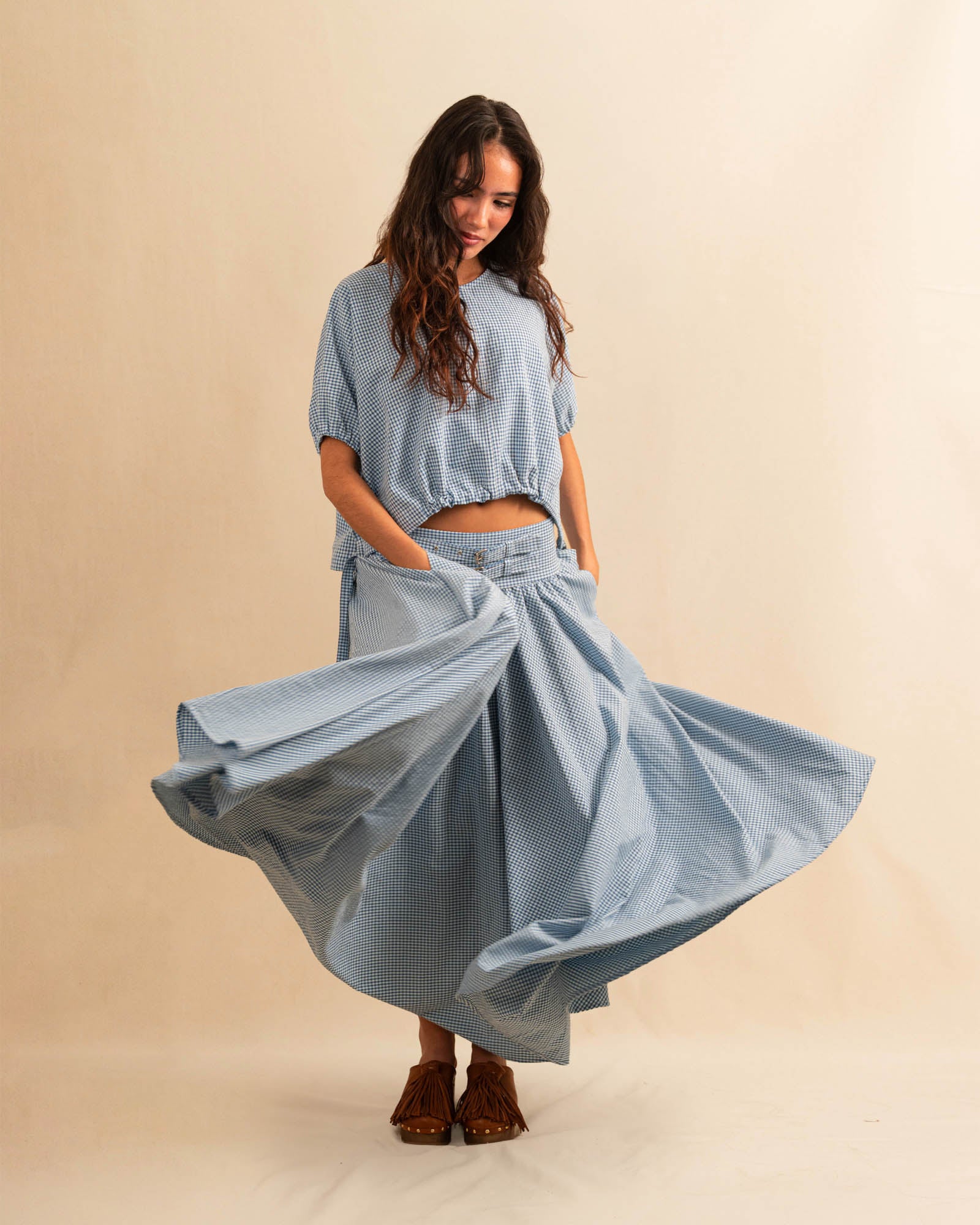 Der Skirt CRISTY von LABEL17 in einem klassischen Blau-Weiss Vichy-Karo-Muster fällt in einer weiten Maxi-Länge und verleiht jedem Look eine feminine Leichtigkeit. Zwei Zierschnallen im Bund setzen einen eleganten Akzent. Reissverschluss vorne und elastischer Bund hinten sorgen für angenehmen Tragekomfort.