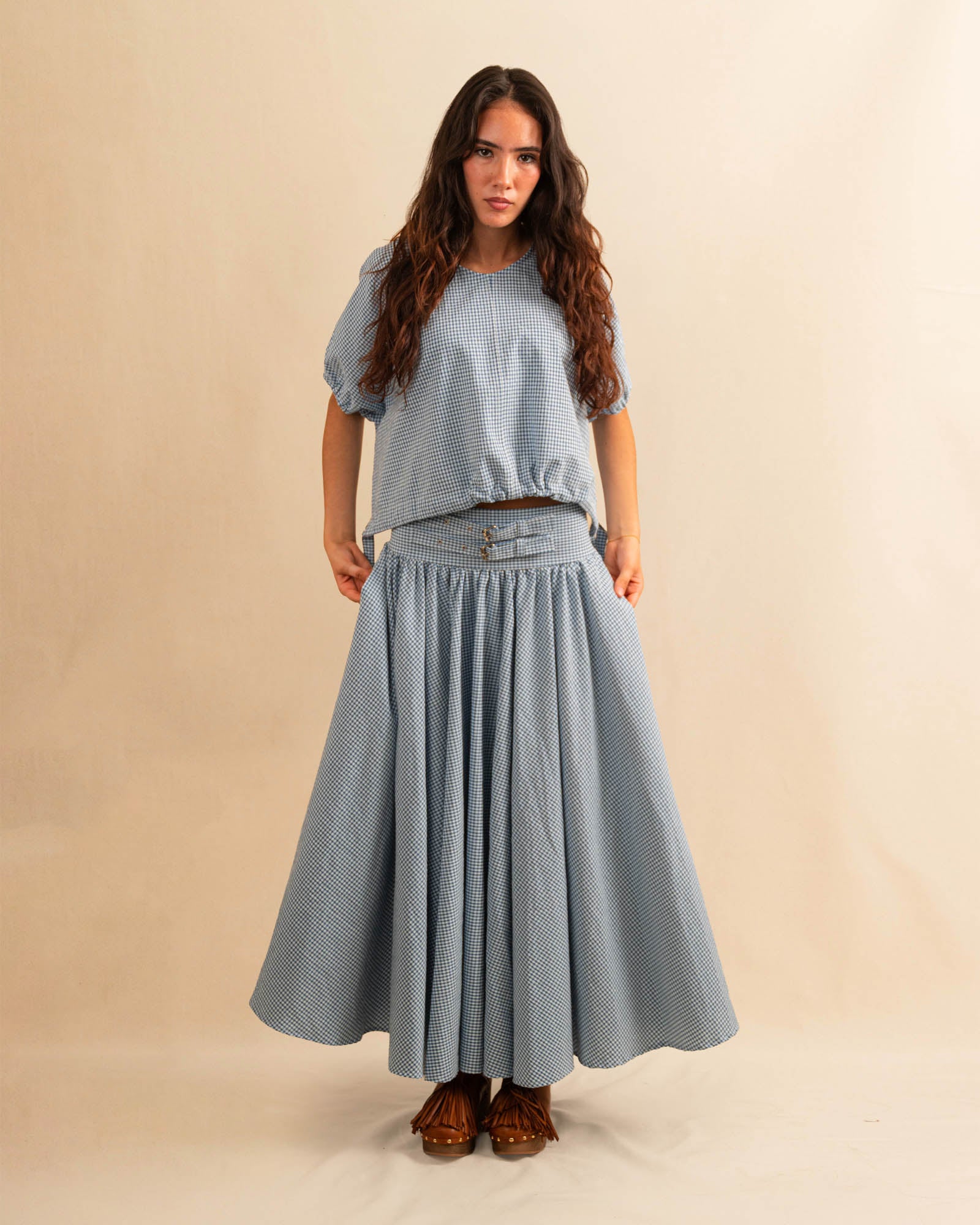 Der Skirt CRISTY von LABEL17 in einem klassischen Blau-Weiss Vichy-Karo-Muster fällt in einer weiten Maxi-Länge und verleiht jedem Look eine feminine Leichtigkeit. Zwei Zierschnallen im Bund setzen einen eleganten Akzent. Reissverschluss vorne und elastischer Bund hinten sorgen für angenehmen Tragekomfort.