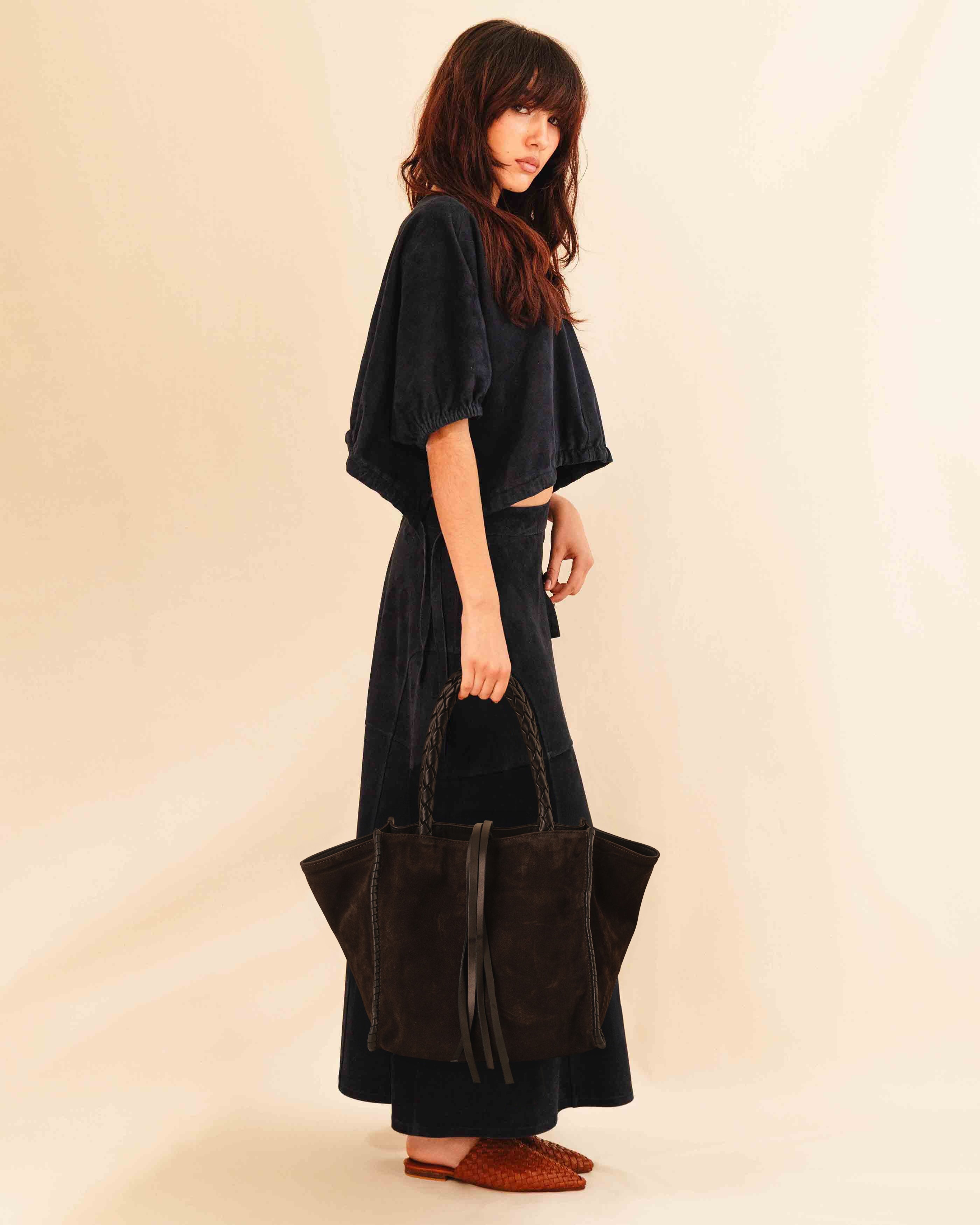 Die Shoulder Bag IVY von LABEL17 ist aus geschmeidigem Velours-Leder gefertigt und zeichnet sich durch handwerkliche Details wie markante Seitennähte und lange, geflochtene Henkel aus. Mit den Lederbändern lässt sich die Tasche elegant zuschnüren – eine gelungene Verbindung von Funktion und Raffinesse.