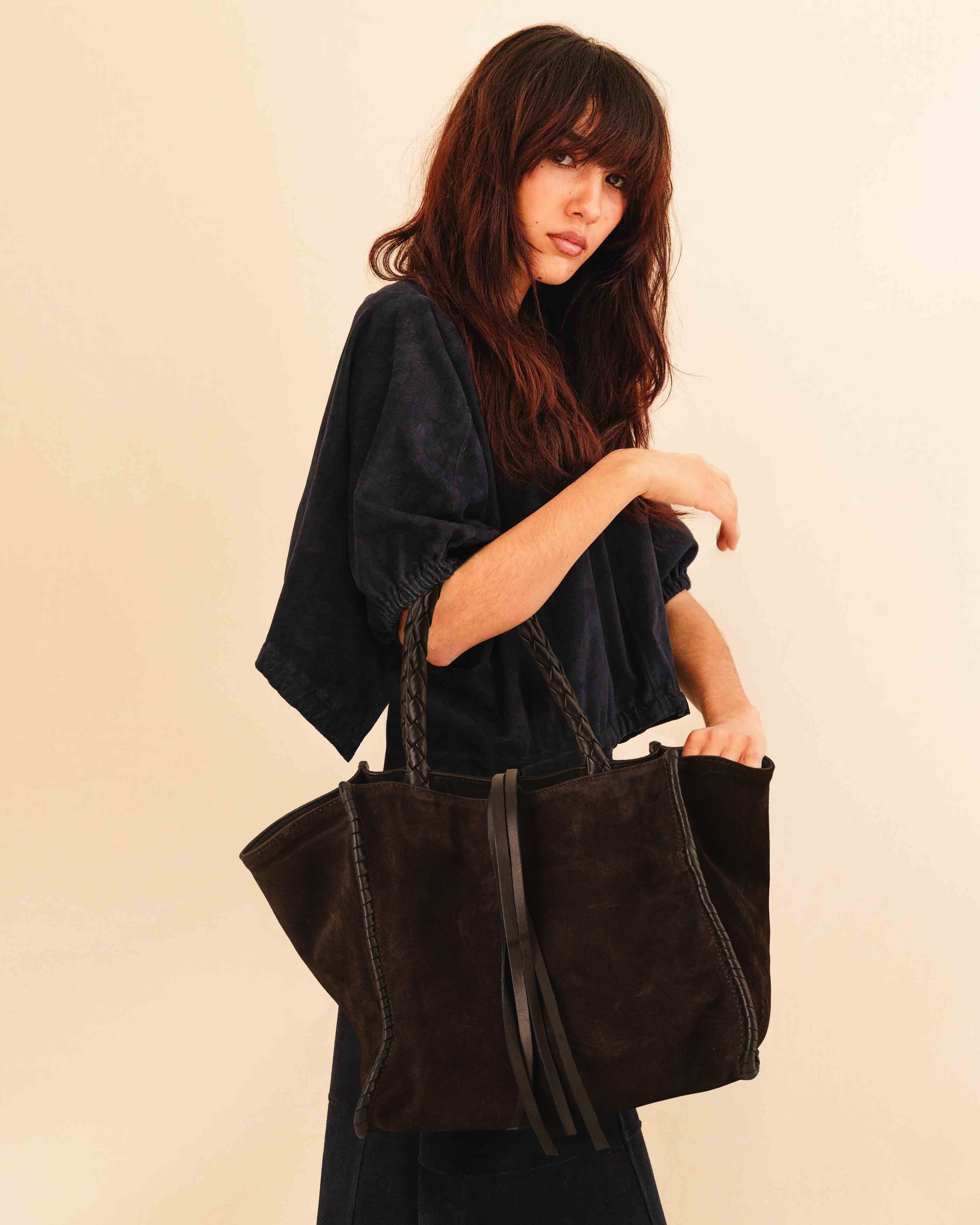 Die Shoulder Bag IVY von LABEL17 ist aus geschmeidigem Velours-Leder gefertigt und zeichnet sich durch handwerkliche Details wie markante Seitennähte und lange, geflochtene Henkel aus. Mit den Lederbändern lässt sich die Tasche elegant zuschnüren – eine gelungene Verbindung von Funktion und Raffinesse.